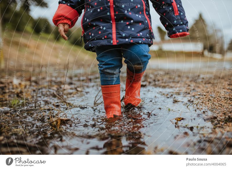 Kind mit roten Gummistiefeln spielt auf einer Pfütze Kindheit Außenaufnahme Wasser Spielen Wetter schlechtes Wetter dreckig Stiefel Farbfoto Tag Freude Herbst