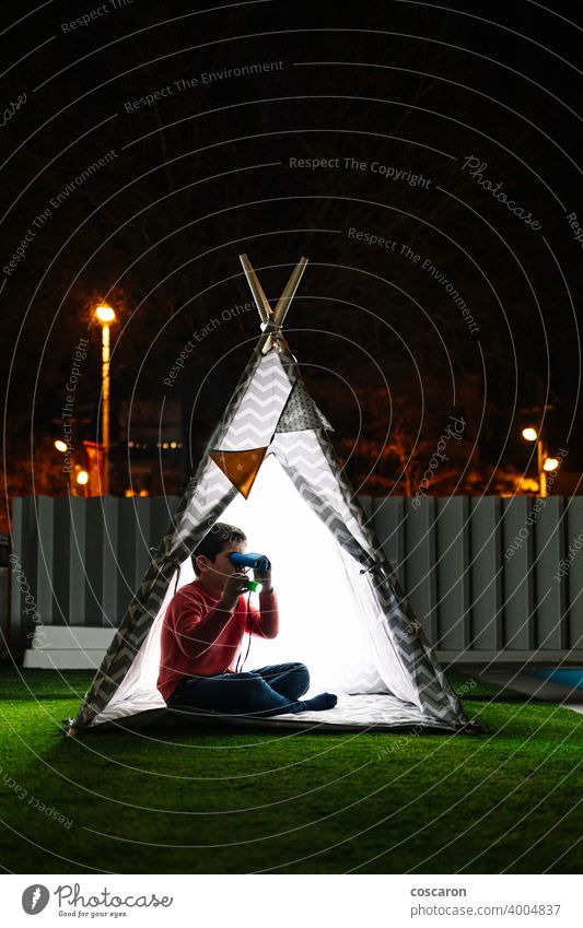 Kleines Kind mit einem Fernglas auf einem indischen Zelt in der Nacht Abenteuer Junge Lager Kerzen Kindheit Kinder dunkel Abenddämmerung genießend erkundend