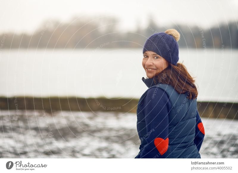 Glückliche brünette Frau mittleren Alters im Pullover mit Strickmütze dreht sich um und schaut in die Kamera sich[Akk] wandelnd Gesicht Porträt Winter Lächeln