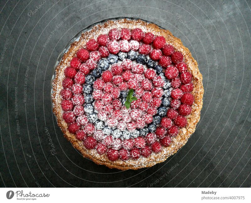 Leckerer Obstkuchen mit Himbeeren, Brombeeren und Puderzucker auf dunkelgrauem Betonboden in einer Designerwohnung in Rottenbuch im Kreis Weilheim-Schongau in Oberbayern