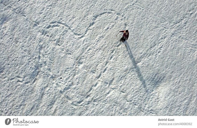 Luftaufnahme mit einer Drohne von einer Schneeschuläuferin die eine Spur in Form von einem Herz in den Schnee gelaufen hat luftaufnahme frau sport winter schnee