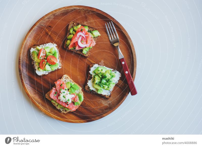 Leckeres Diätessen zum Frühstück oder Brunch - Avocado- und Lachstoast mit Frischkäse, Gurke und roter Zwiebel auf Holzteller serviert Lebensmittel