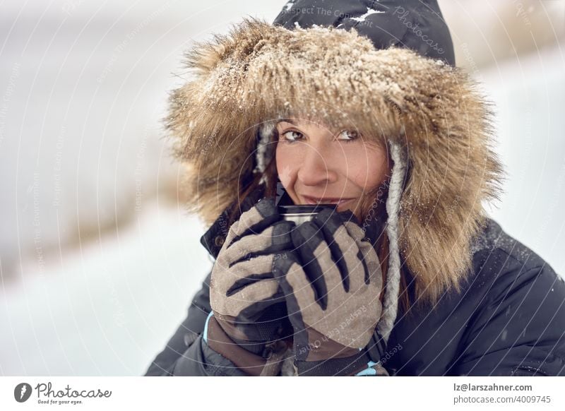 Glücklich lächelnde Frau trägt einen Pelz getrimmt Kapuzenjacke genießen einen Becher Kaffee in ihren behandschuhten Händen im Freien im Winter Schnee in einem Konzept der Jahreszeiten in einer Nahaufnahme Porträt Wiegen