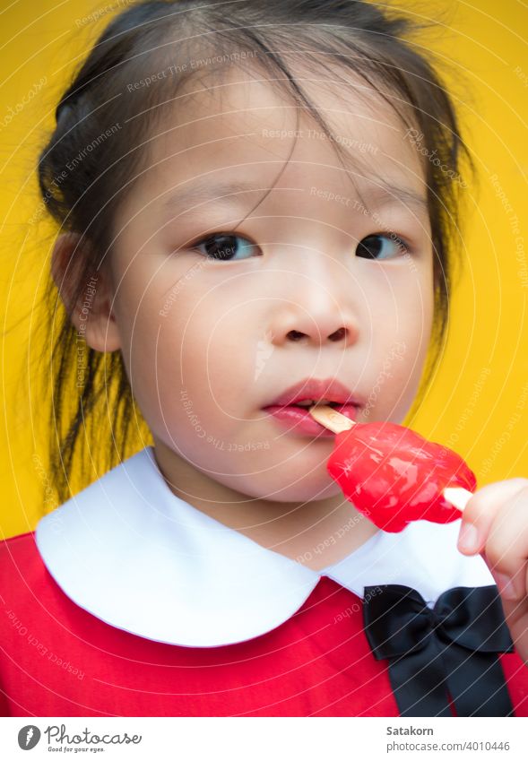 Kleine Mädchen in rot Student gekleidet Essen ein rotes Eis am Stiel Stieleis wenig niedlich süß essen jung Hintergrund Lebensmittel Glück Spaß Dessert Sahne