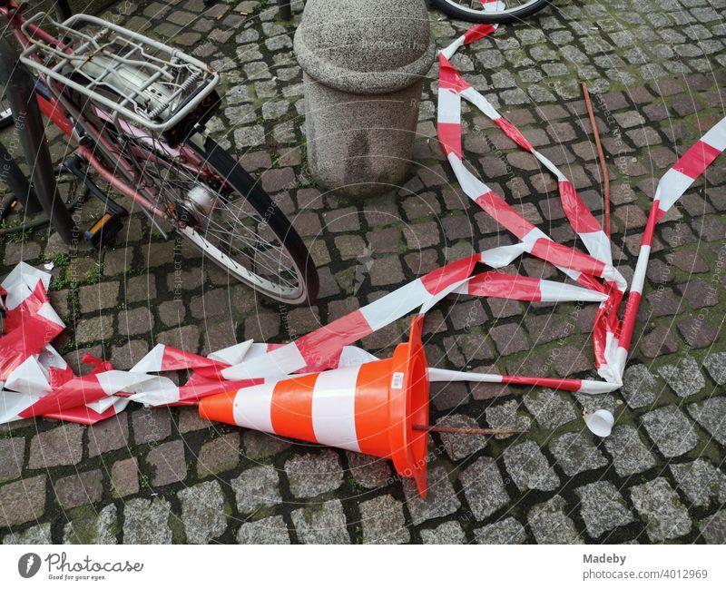 Umgeworfenes Lübecker Hütchen und abergerissenes Absperrband in Rot und Weiß auf Kopfsteinpflaster in der Innenstadt von Frankfurt am Main in Hessen Kegel