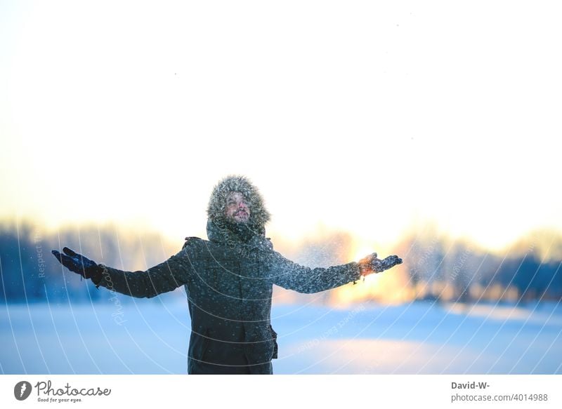 es schneit - Mann freut sich über den Schnee im Winter winterlich freude Sonnenlicht Sonnenuntergang Spaß hochwerfen Schneefall verschneit Wintertag