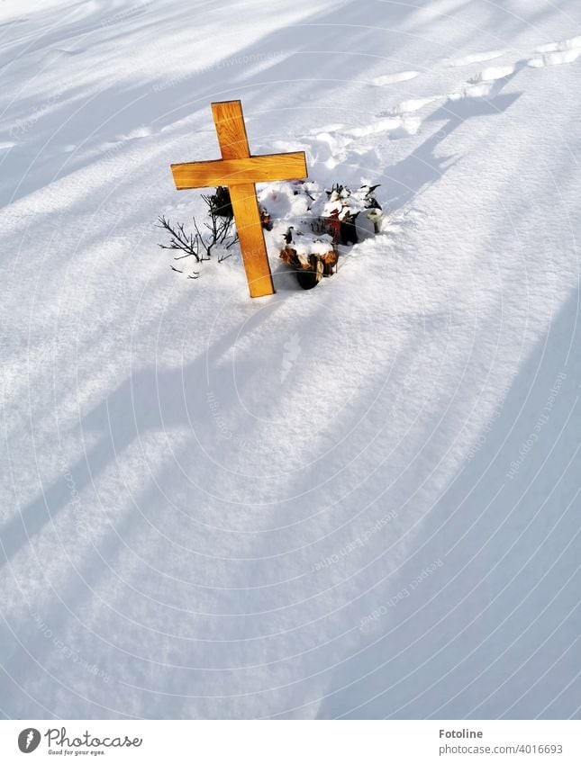 Zugeschneites Grab auf einem Friedhof. Das Kreuz wirft lange Schatten. Winter Schnee Schneedecke verschneit kalt weiß Winterstimmung Wintertag Außenaufnahme