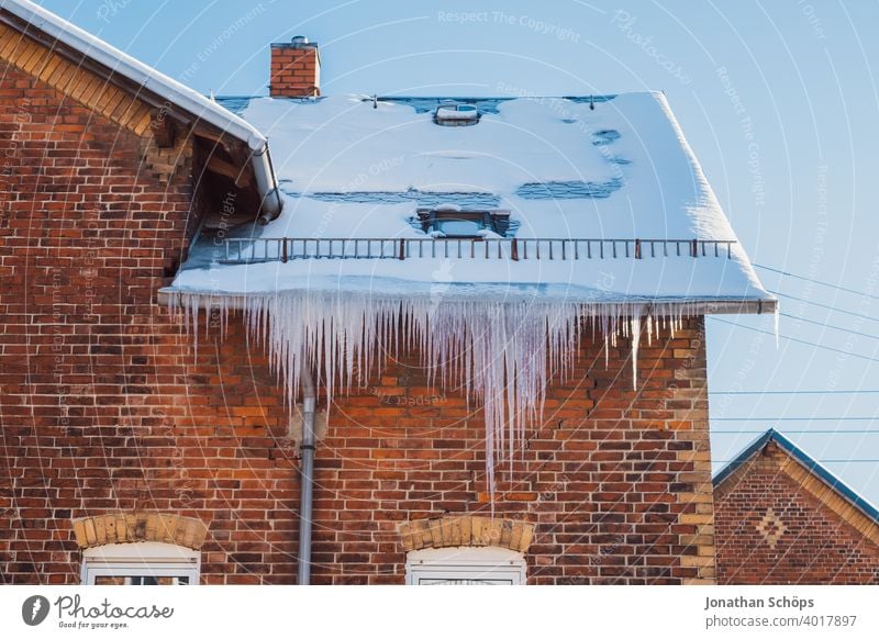 lange Eiszapfen an Dachrinne eines Backsteinhauses im Winter bei eisiger Kälte und Sonne architektur backstein Backsteinhaussiedlung Dachkante dachrinne