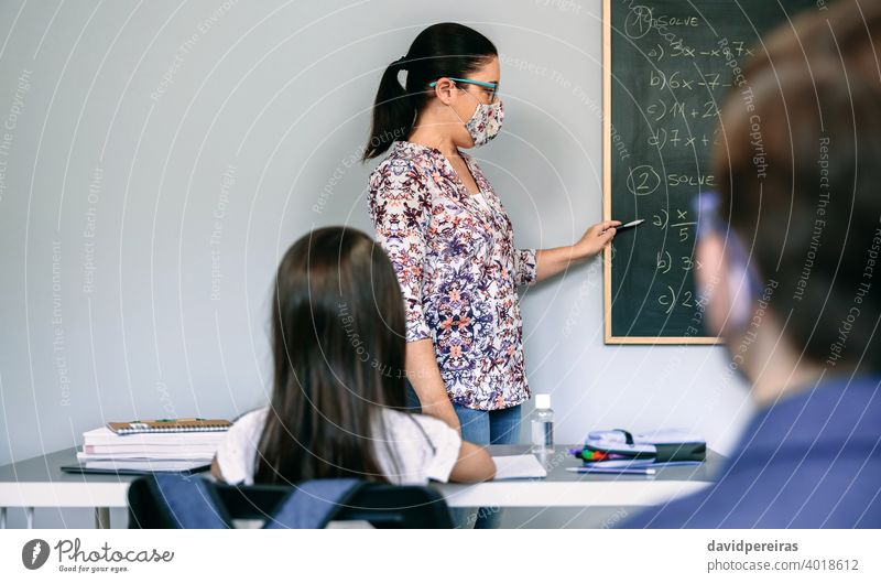 Lehrer mit Maske erklärt Übungen im Matheunterricht Lehrerin zu erklären. Schutzmaske neue Normale Schüler covid-19 Tafel Schule Zeigen Textfreiraum Sicherheit