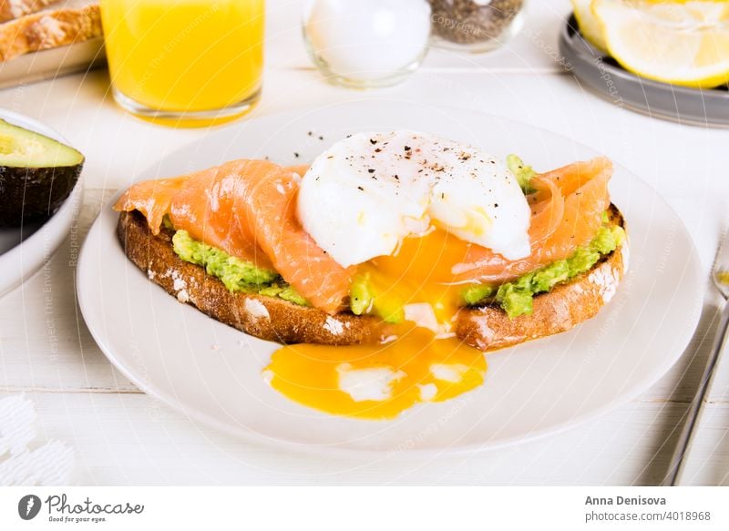 Vollkornbrottoast, zerdrückte Avocado, Lachs und pochiertes Ei Frühstück gekocht Zuprosten Brot grün Entzug Diät Zitrone Clementine Fisch Saft Glas Tasse