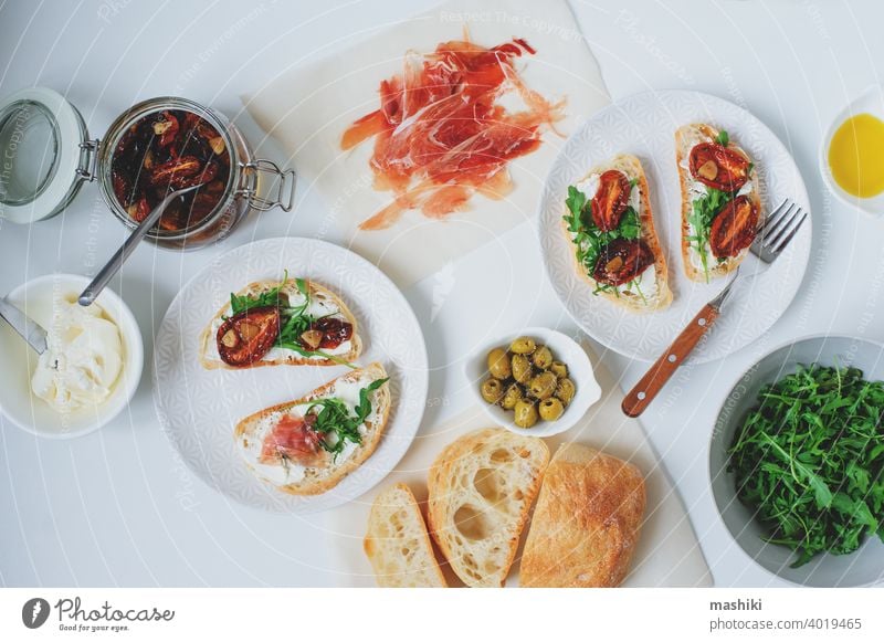 traditionelle italienische Bruschetta - Brottoast mit sonnengetrockneten Tomaten, Frischkäse, Olivenöl und Rucola. Belegtes Brot Lebensmittel Zuprosten Snack