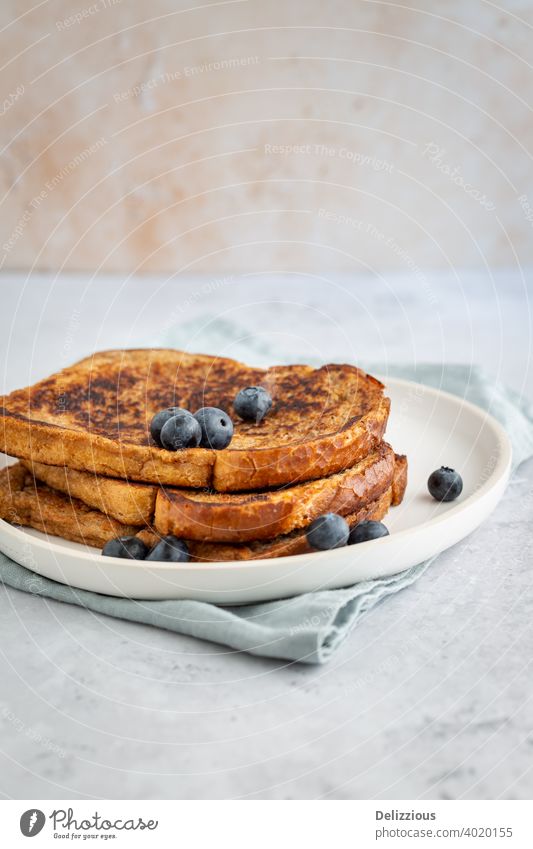 Seitenansicht von drei Scheiben köstlichen French Toast mit Blaubeeren auf einem Teller auf grauem Hintergrund, minimalistischen Stil mit Kopie Raum goelteefjes