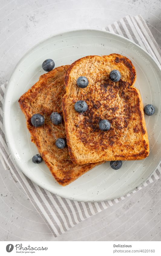 Nahaufnahme von oben von drei leckeren Scheiben French Toast mit Blaubeeren auf einem Teller auf grauem Hintergrund, minimalistischen Stil goelteefjes Zutaten