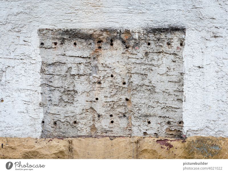 Hauswand mit Bohrlöchern und Umriss eines Kaugummiautomaten Wand Mauer Häuserwand Löcher Bohrungen Wandfarbe Farbe weiß Sockel Außenaufnahme Fassade Farbfoto