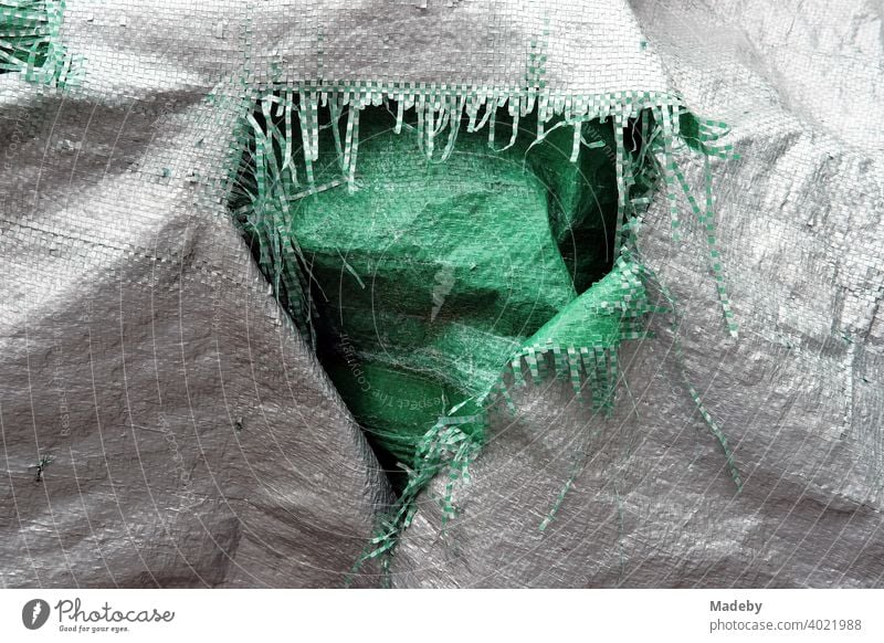 Aufgerissene Kunststoffplane mit Fasern in Grau und Grün in einem Garten in Rudersau bei Rottenbuch im Kreis Weilheim-Schongau in Oberbayern Plane Abdeckung