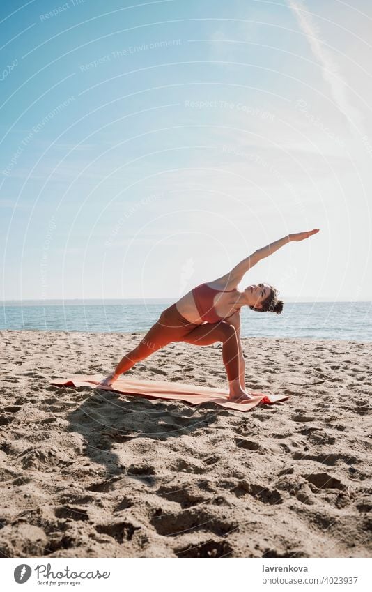 Junge Frau in orangefarbenem Oberteil und Leggins beim Üben der Erweiterten Seitenwinkelstellung (Utthita Parsvakonasana) Übung Pose Yoga Strand jung