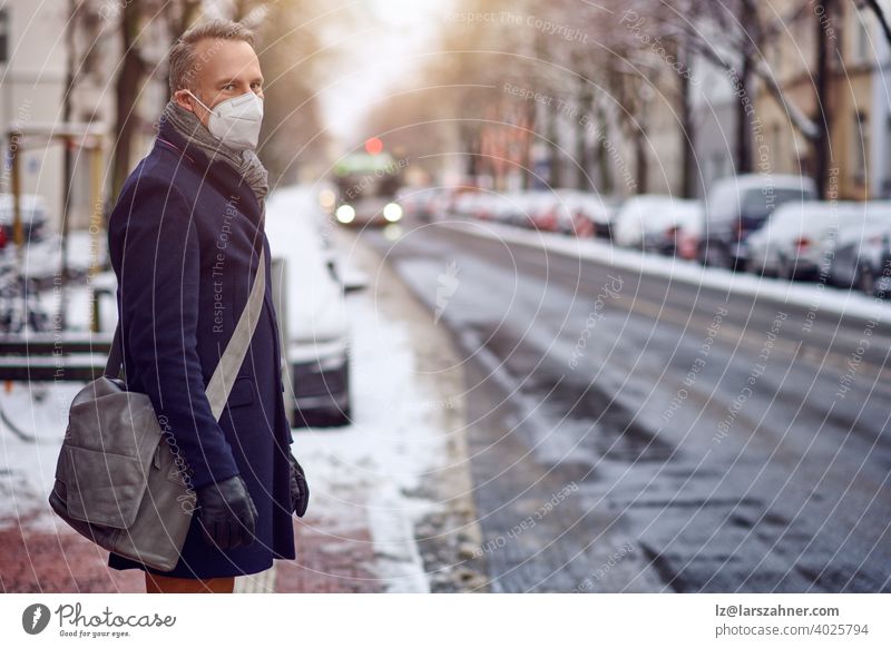 Brünette Frau mittleren Alters, die an einer Bushaltestelle steht, eine schützende Gesichtsmaske aufgrund des Coronavirus trägt und auf ihren Bus wartet, der sie zur Arbeit bringt