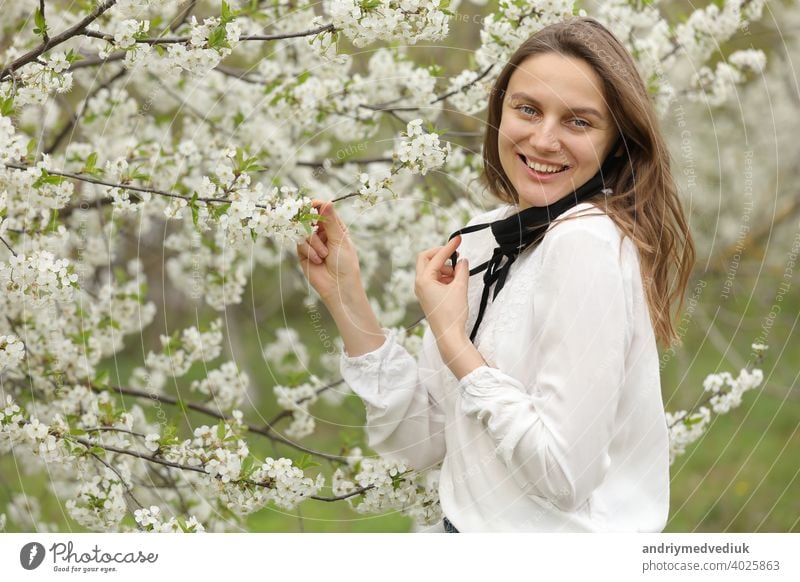 frau nahm ihre maske ab, um den duft der blumen einzuatmen. mädchen berührt den blühenden kirschbaumzweig im garten mit den händen an einem frühlingstag. schönes mädchen in einer kirschblüte.