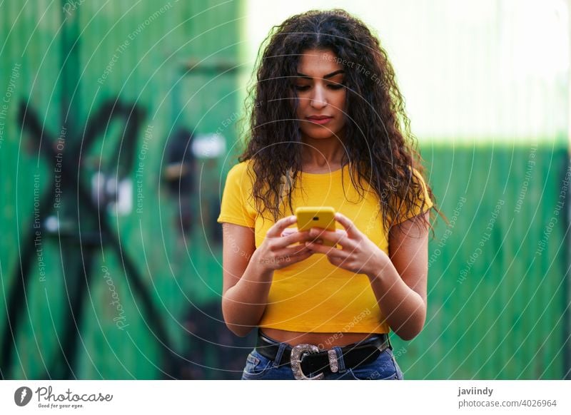 Junge arabische Frau geht auf der Straße mit ihrem Smartphone jung Texten Nachricht Tippen gelb copyspace Mädchen Aufnahme Frisur attraktiv schön urban