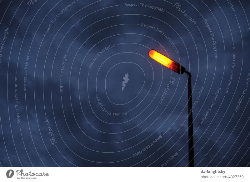 Orangefarbenes Licht auf einer Laterne vor blau-grauem Himmel mit dichten Wolken Sicherheit planen Freiraum Textfreiraum Froschperspektive Stadtraum