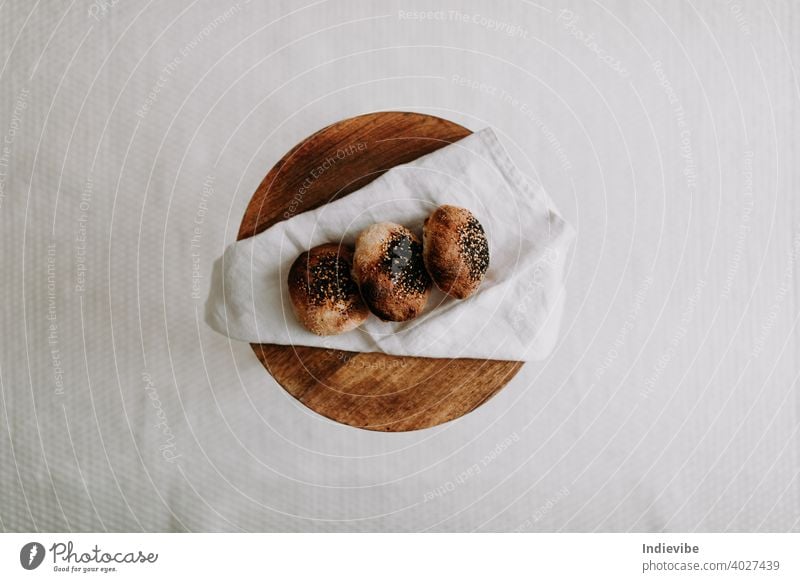 Drei Sauerteigbrötchen flachgelegt mit Mohn und Sesam auf einer Serviette auf einem Holzhocker Brötchen Frühstück Brot Gluten Gebäck Bäckerei frisch Morgen Mehl