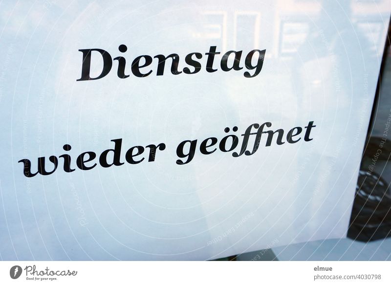 ein schlichter weißer Zettel hinter einer Schaufensterscheibe mit der Aufschrift "Dienstag wieder geöffnet" Öffnungszeit Mitteilung Ladenöffnungszeiten Telefon