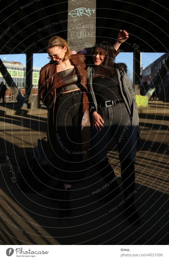 Lara und Estila frau langhaarig stehen cool freundschaft mantel lässig blond dunkelhaarig architektur brücke sonnig sonnenlicht miteinander beieinander zusammen