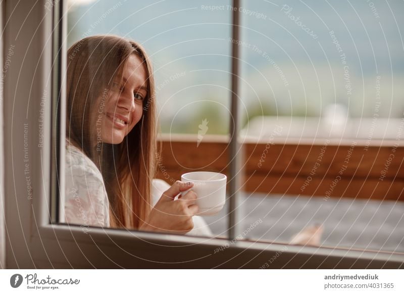 Junge Frau stehend nach dem Duschen am Morgen auf dem Balkon des Hotels. hält eine Tasse Kaffee oder Tee in ihren Händen. Blick nach draußen Natur Wald und Berg