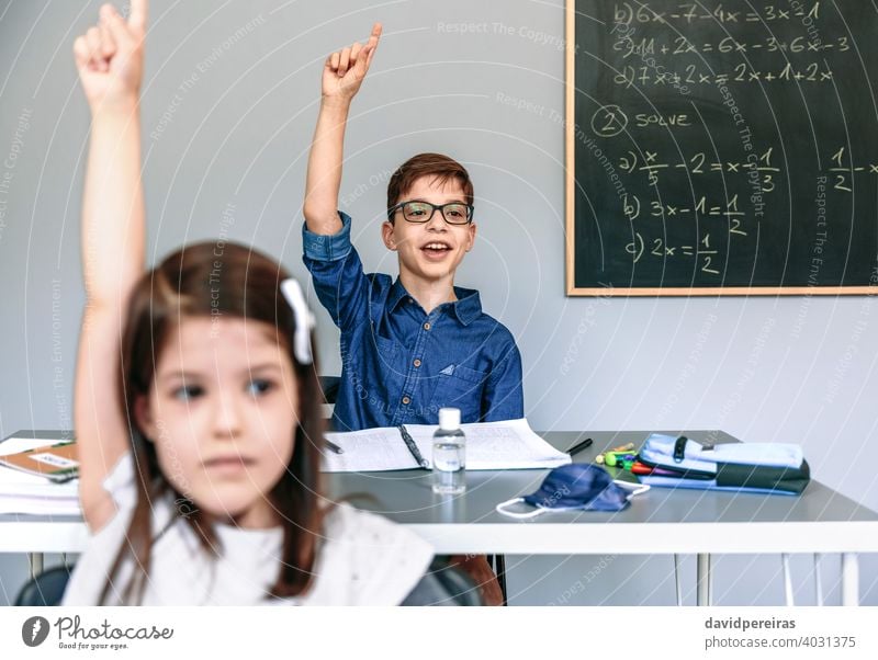 Schüler mit Maske auf dem Tisch heben die Hände in der Schule Junge Handreichung sprechend fragen Coronavirus Klasse teilnehmend Sicherheit Virus neue Normale