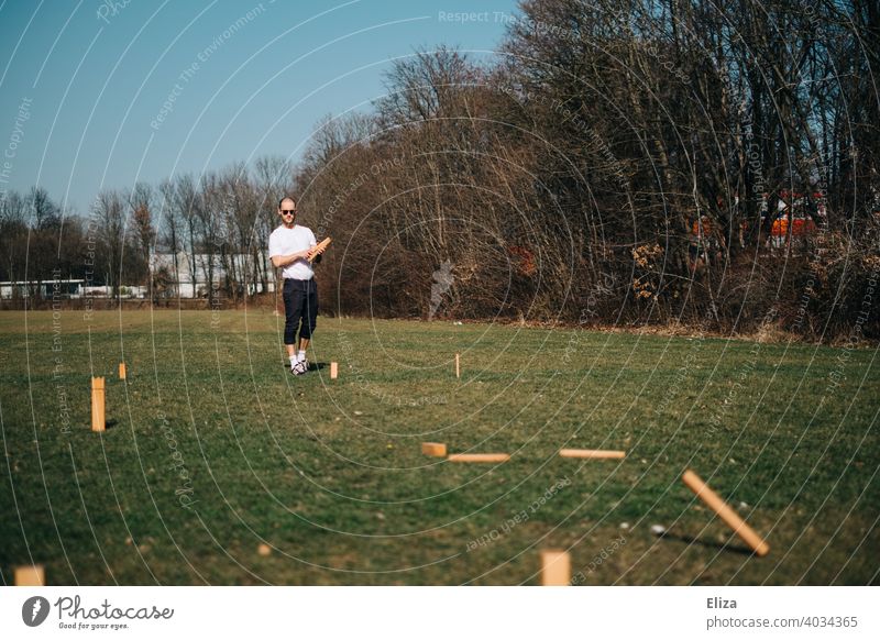 Ein Mann beim Wikingerschach/Kubb spielen draußen auf der Wiese werfen Spiel Aktivität Freizeit aktiv Frühling Sommer Sonne im Freien