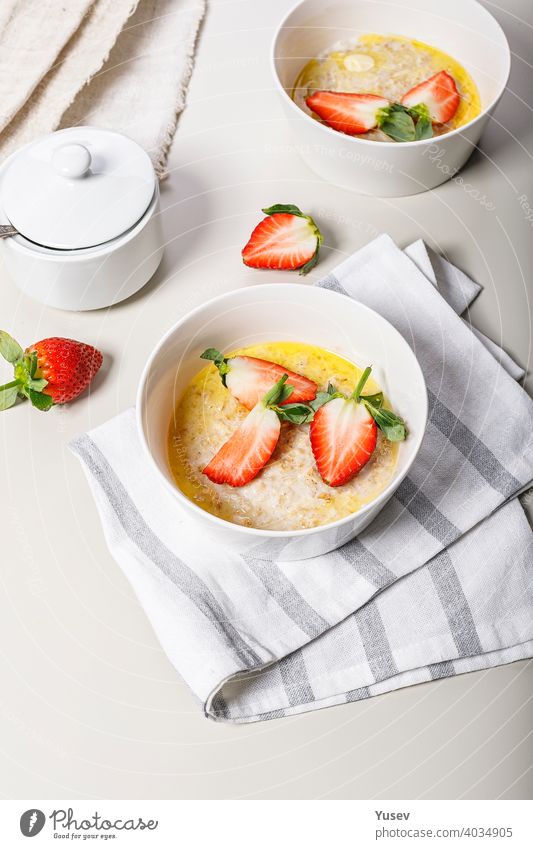 Klassische Haferflocken mit Butter und frischem Obst. Süße Erdbeeren. Leckeres und gesundes Frühstück. Essen Stillleben auf einem hellen Hintergrund. Ideen und Rezepte für Hausmannskost. Vertikale Aufnahme