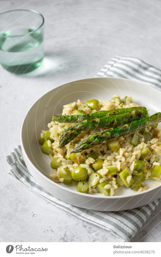 Leckeres Risotto mit gegrilltem Spargel auf weißem Teller, grauer Hintergrund, vertikal mit grünem Glas Grünspargel Lebensmittel Seitenansicht Rezept