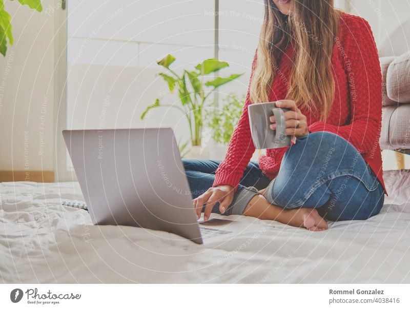 Eine Frau, die Tee trinkt, auf dem Boden einer Wohnung sitzt und sich Notizen macht, hat einen Laptop vor sich aufgeklappt. Home-Office-Konzept. Bietet Kaffee an. Konzept kreative Arbeit zu Hause. Selektiver Fokus.