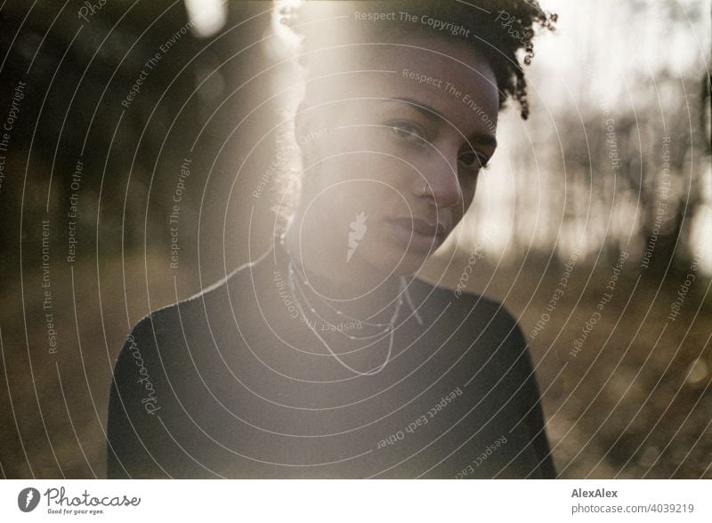 Junge Frau steht in der Natur an einem See - analoges Gegenlicht- Portrait sportlich dunkelhaarig langhaarig hübsch stark zierlich natürlich lockig schlank Aus