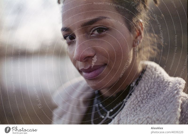 Junge Frau steht in der Natur an einem See  - analoges  Portrait sportlich dunkelhaarig langhaarig hübsch stark zierlich natürlich lockig schlank Aus Schmuck