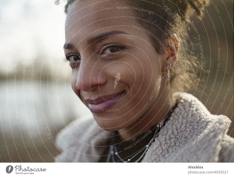 Junge Frau steht in der Natur an einem See und lächelt - analoges  Portrait sportlich dunkelhaarig langhaarig hübsch stark zierlich natürlich lockig schlank Aus