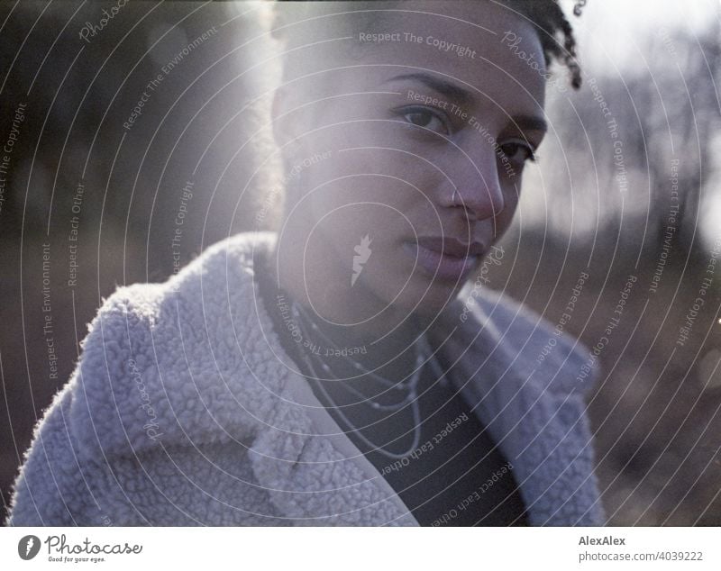 Junge Frau steht in der Natur an einem See - analoges Gegenlicht- Portrait sportlich dunkelhaarig langhaarig hübsch stark zierlich natürlich lockig schlank Aus