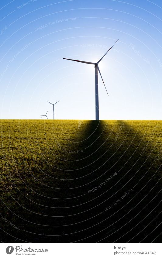 Windkraftanlagen auf dem Feld im Gegenlicht vor blauem Himmel. Schattenwurf von Mast, Sonne hinter dem Generator regenerative energie Erneuerbare Energie