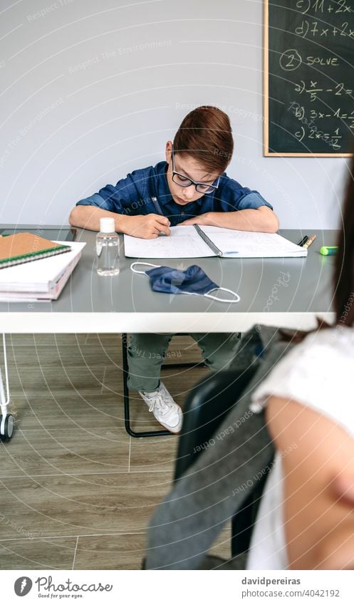 Junge schreibt in der Schule in sein Notizbuch Kind Schüler Klassenraum keine Maske covid-19 Sicherheit Handdesinfektionsmittel schreibend Virus Menschen Seuche