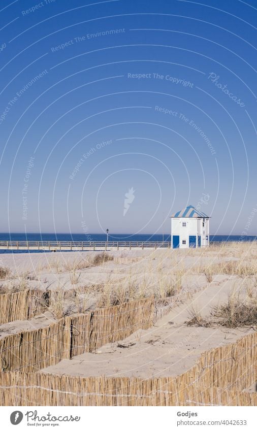 Holzhaus für die Wasserwacht und Brücke hinter einer Düne mit Absperrungen aus Schilf am Strand Abenteuer Panorama (Aussicht) mehrfarbig Stranddüne himmelblau