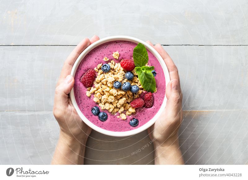 Weibliche Hände halten Smoothie-Bowl mit Granola und Beeren. Schalen & Schüsseln Frühstück Gesundheit Blaubeeren Himbeeren Hand Beteiligung Tisch Joghurt