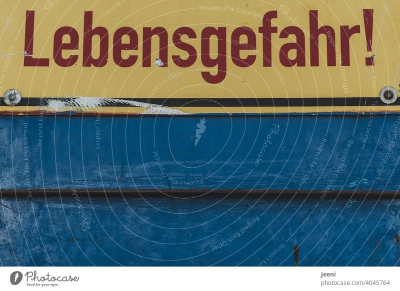 "Lebensgefahr" geschrieben in roten Buchstaben auf einem gelben Schild auf blauem Hintergrund | sich dort hinein zu begeben ist ziemlich „ungesund“ gefährlich