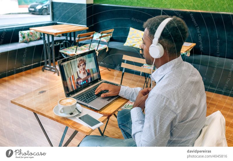 Mann spricht per Videoanruf mit seiner Großmutter sprechend Laptop Café Internet Kopfhörer Bildschirm Person Videokonferenz männlich Mutter Tisch Familie Sitzen