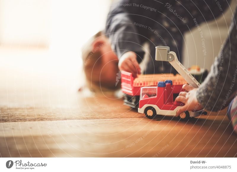 Kinder spielen mit ihrem Spielzeug auf einem Holzboden zusammen Spaß gemeinsam Geschwister zu Hause Familie Kindheit