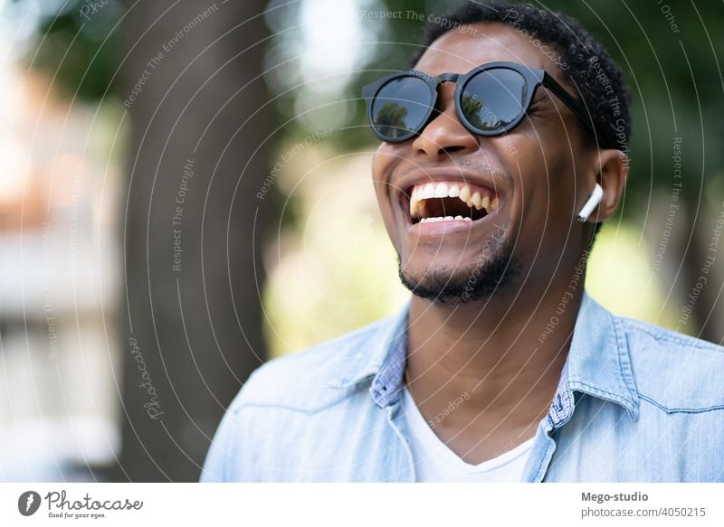 Afroamerikanischer Mann lächelnd beim Gehen im Freien. Afrikanisch Amerikaner Sonnenbrille Großstadt urban Konzept laufen Ohrhörer Lächeln Freude Freizeit