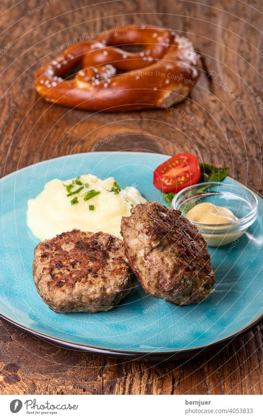 zwei Fleischpflanzerl einem Teller bulette senf kartoffelpüree kartoffelbrei breze brezel bayerisch rustikal deftig holz tomate snack brotzeit hackfleisch