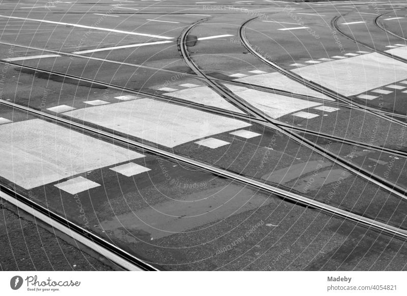 Abzweigende Straßenbahnschienen mit Radweg, Fußgängerüberweg und anderen Straßenmarkierungen auf grauem Asphalt in der Innenstadt von Frankfurt am Main in Hessen, fotografiert in klassischem Schwarzweiß