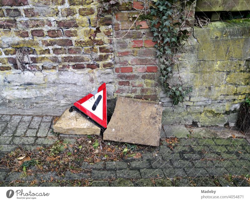 Kaputtes Warndreieck mit großen Steinen am Straßenrand auf altem Kopfsteinpflaster vor Mauerwerk im Herbst in der Altstadt von Oerlinghausen bei Bielefeld im Teutoburger Wald in Ostwestfalen-Lippe