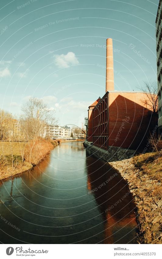 Ein sonniger Tag am ruhigen Fluss, an dessen Ufer eine Fabrik mit Schornstein steht. Time meint, die kleinen Wölkchen sollten auch erwähnt werden.