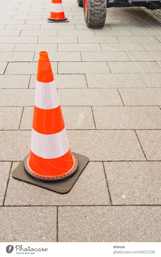 In einer Fußgängerzone sperren rot-weiße Pylone eine Baustelle ab - ein Teil des Baggers ist sichtbar / Bauarbeiten / Markierungshütchen / Sicherheit